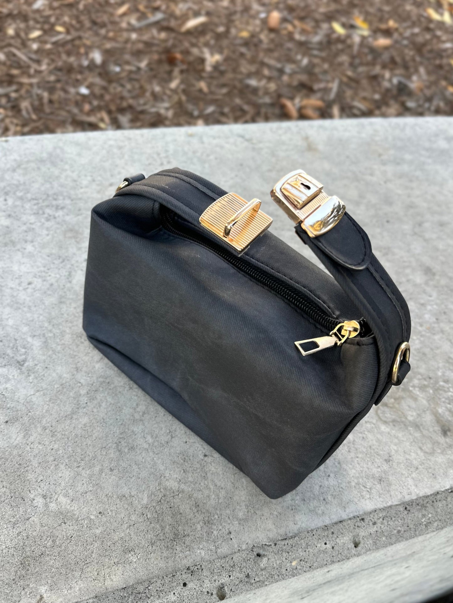 Black handbag with gold accents on a concrete surface