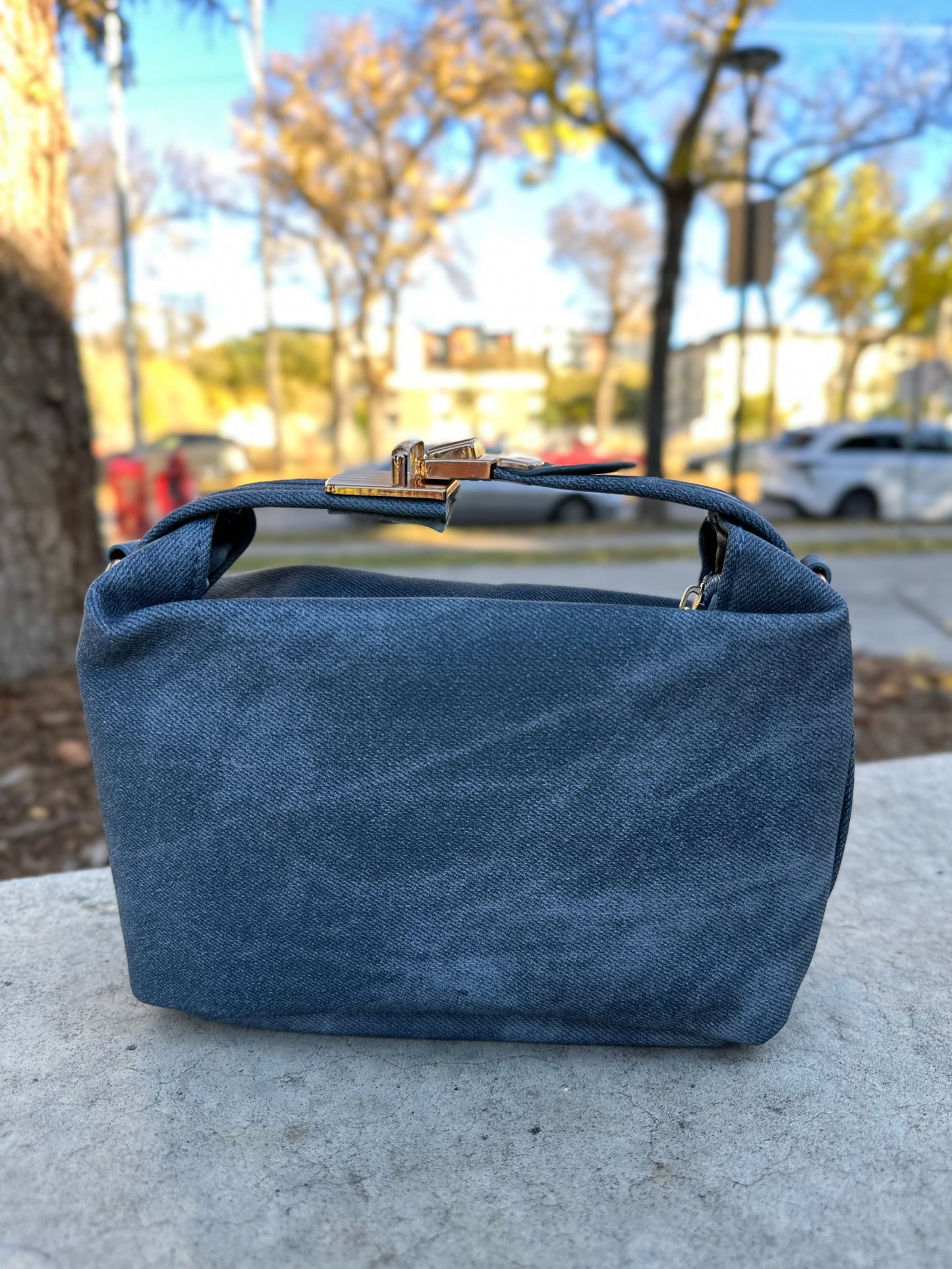 Blue denim bag on a concrete surface with a blurred outdoor background